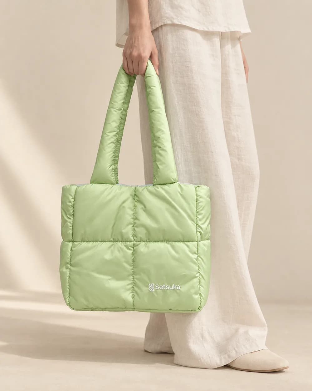 Tay xách túi chần bông xanh bơ bên hông, quần linen ống rộng màu trắng ngà